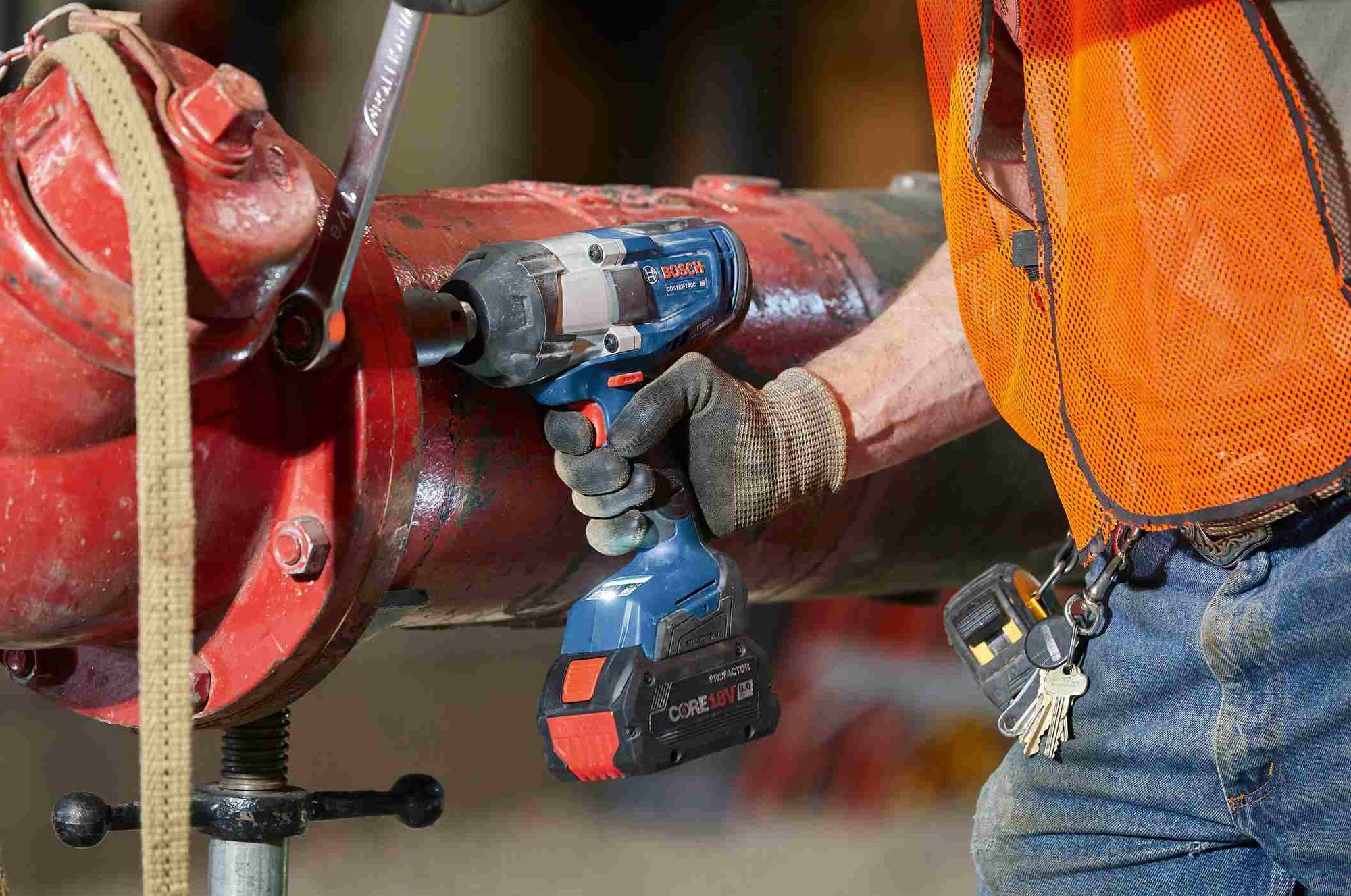 A worker using a Bosch impact wrench on a large, red pipe.