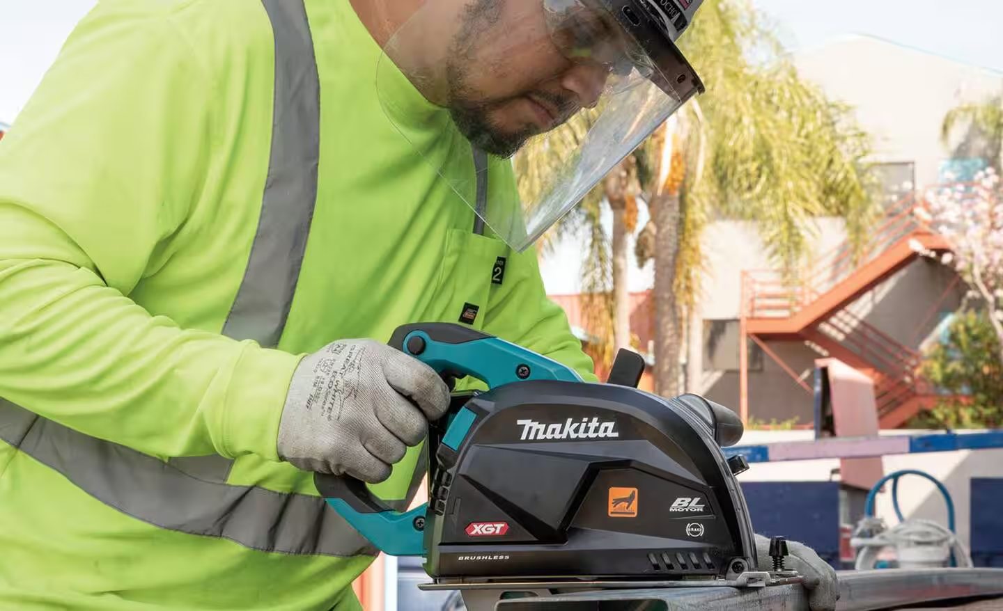 A worker in safety equipment using a Makita power circular saw.
