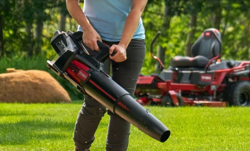 Man using an outdoor blower in a grassy field.