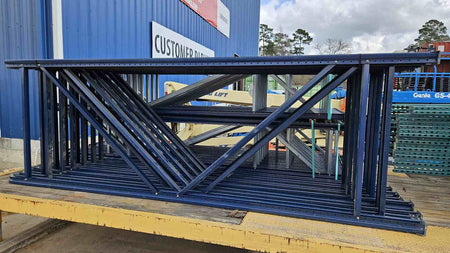 A horizontal stack of used like-new 12-foot industrial blue pallet rack uprights, featuring heavy-duty steel frames with a 48-inch depth, organized on a flatbed trailer for high-capacity warehouse storage system transport.