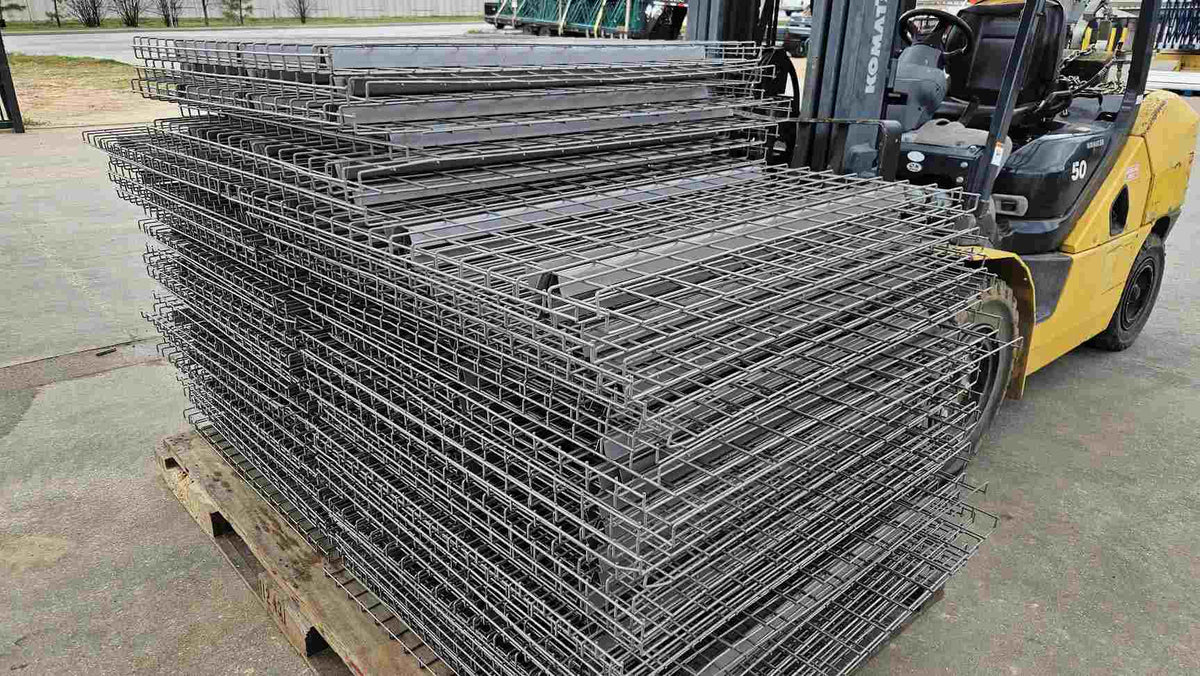 Profile view of a high stack of reinforced steel mesh wire decks for industrial pallet racking systems, showcasing the drop-in safety support design and flared U-channel reinforcements suitable for heavy-duty warehouse equipment storage.