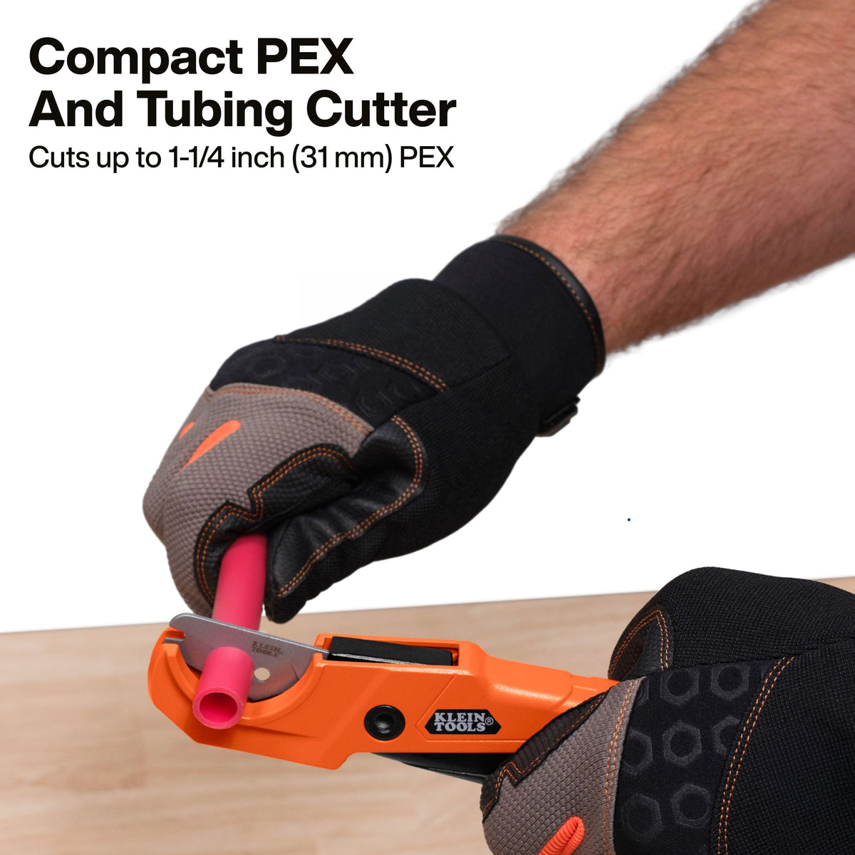 A person wearing black and gray work gloves uses an orange Klein Tools compact PEX and tubing cutter to cut a pink PEX pipe. Text at the top reads 'Compact PEX And Tubing Cutter' and 'Cuts up to 1-1/4 inch (31 mm) PEX'.