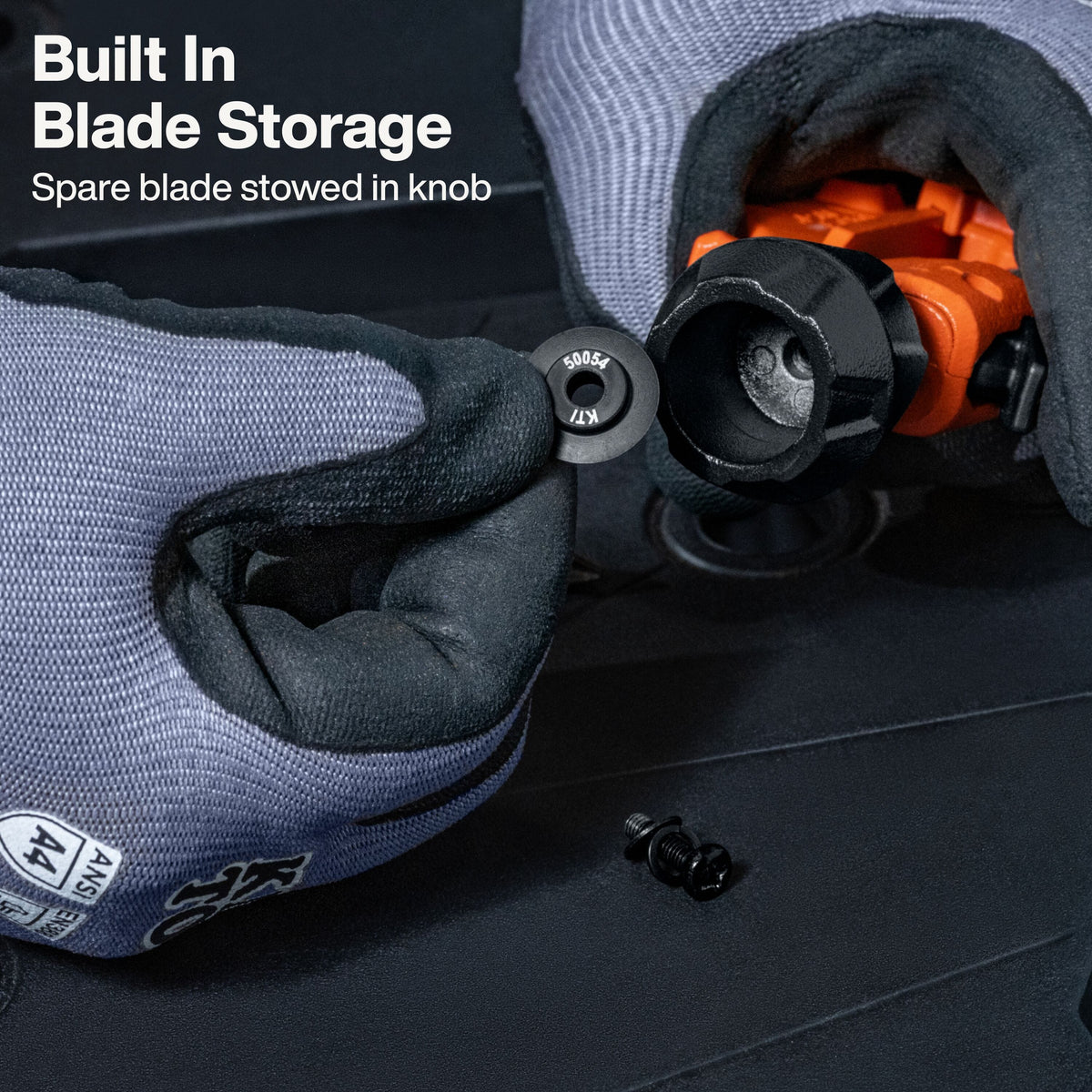 Close-up of gloved hands demonstrating built-in blade storage on a black tool handle, with a spare blade inserted into the knob. White text in the upper left reads 'Built In Blade Storage' and 'Spare blade stowed in knob.