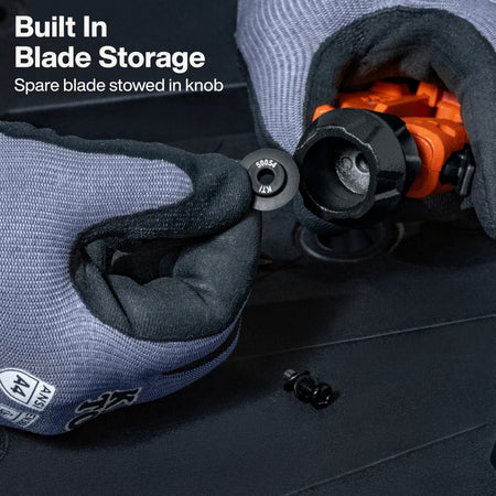 Close-up of gloved hands demonstrating built-in blade storage on a black tool handle, with a spare blade inserted into the knob. White text in the upper left reads 'Built In Blade Storage' and 'Spare blade stowed in knob.