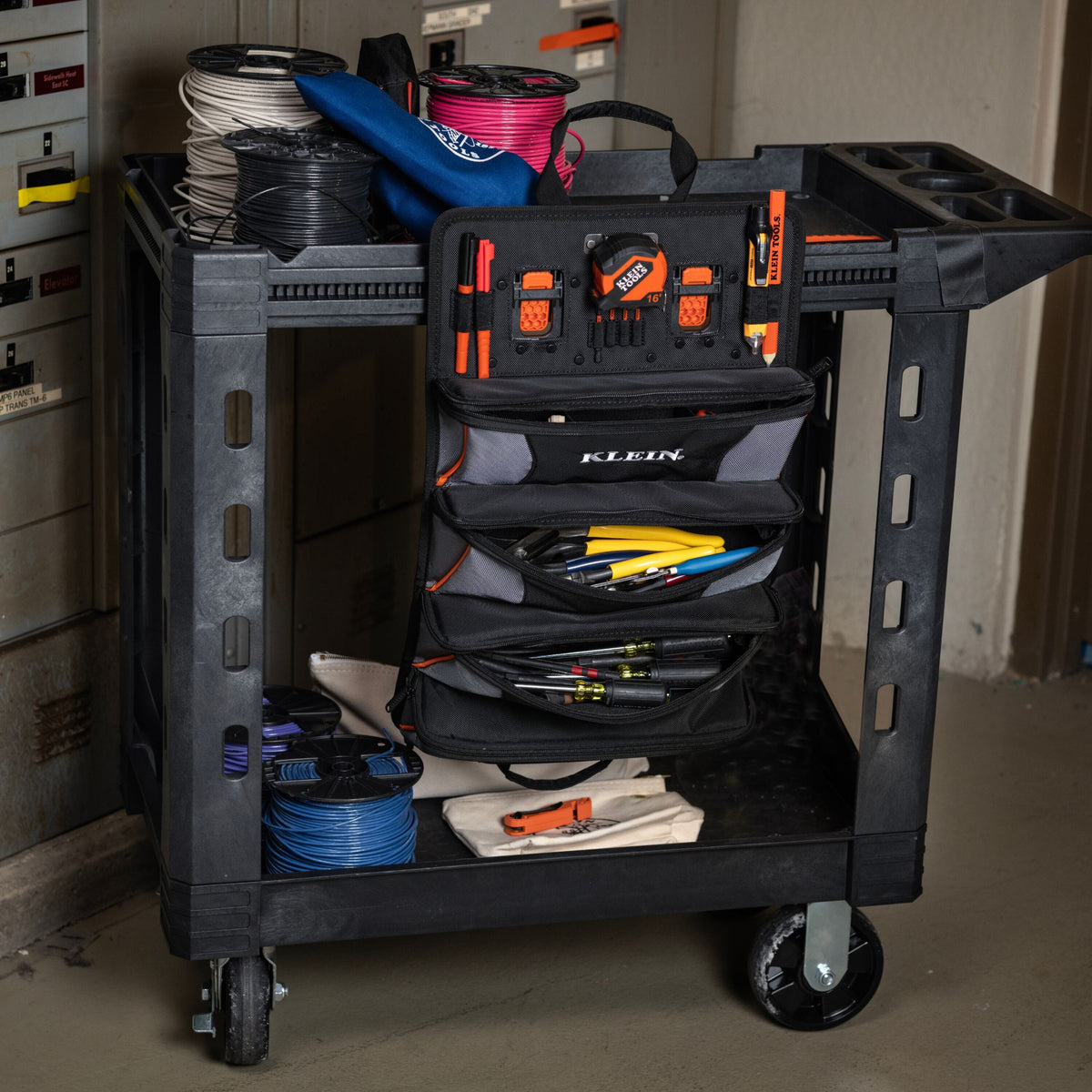 A black Kruuk rolling tool cart filled with electrical tools and wire spools, photographed in a workshop environment.