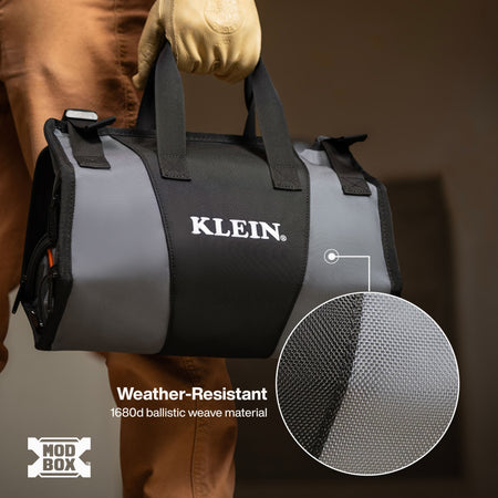 A person wearing a tan work glove holds a black and gray Klein duffel bag with white KLEIN branding. The image includes a circular inset showing a close-up of the weather-resistant mesh material and text reading 'Weather-Resistant 1680d ballistic weave material' with a MOD BOX logo in the corner.