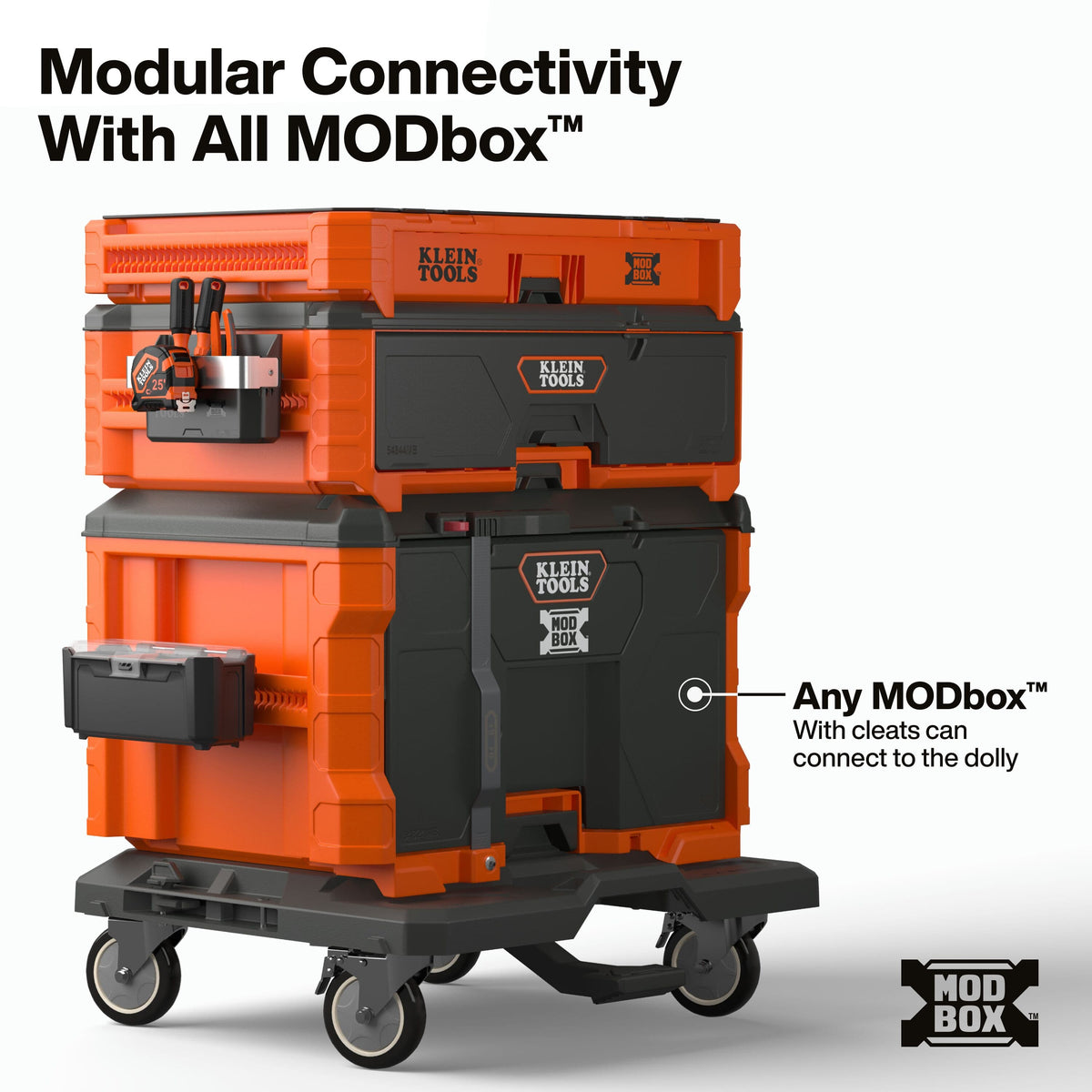 A modular tool storage dolly system by Klein Tools, shown stacked with orange and black plastic toolboxes on a wheeled base. Large text at the top reads 'Modular Connectivity With All MODbox™', and a callout on the right says 'Any MODbox™ with cleats can connect to the dolly.