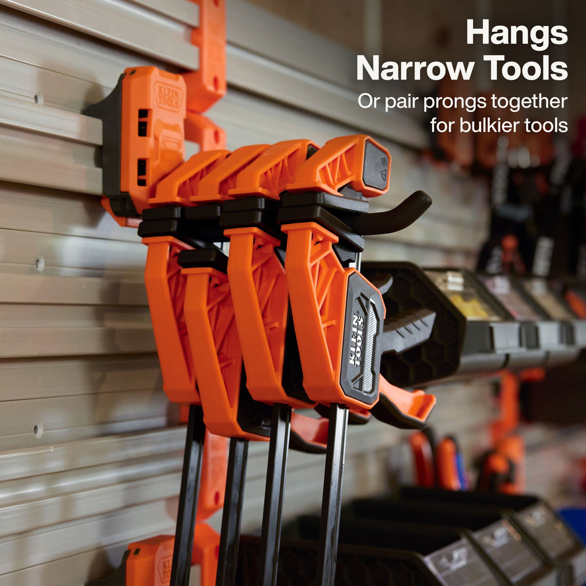 Bright orange and black GCL clamp tools hanging on a gray garage door wall, with white text in the upper right reading 'Hangs Narrow Tools Or pair prongs together for bulkier tools.'.