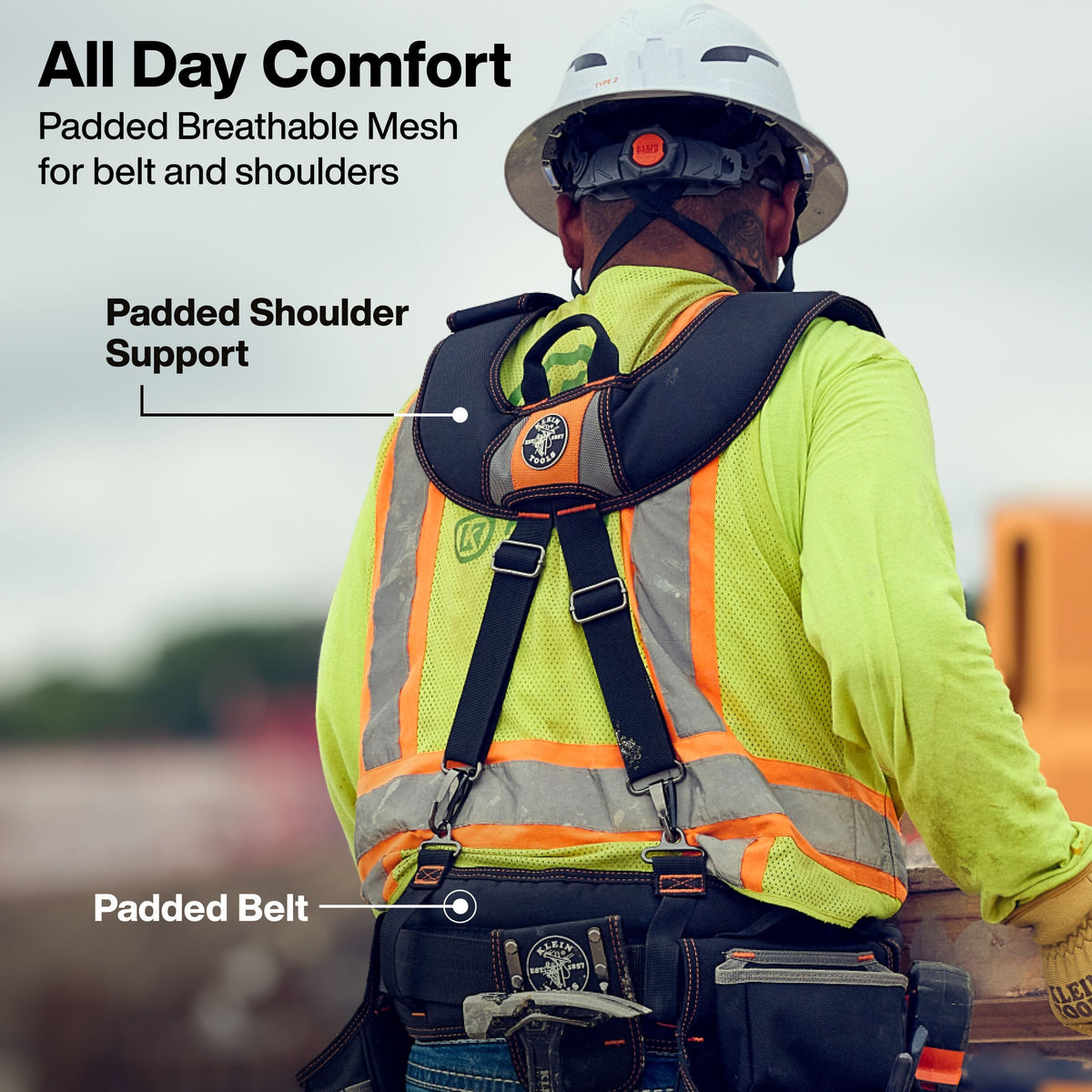 The worker is seen from the back, waist-up, facing away from the camera. They are wearing a white full-brim hard hat with a rear ratchet dial, a bright yellow hi-vis safety vest with orange and silver reflective striping, and leather work gloves. Fitted over the vest is a heavy-duty black and orange suspender harness connected to a thick, loaded padded tool belt at the waist.   