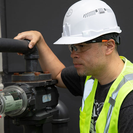Person wearing a white hard hat and safety glasses working on machinery.
