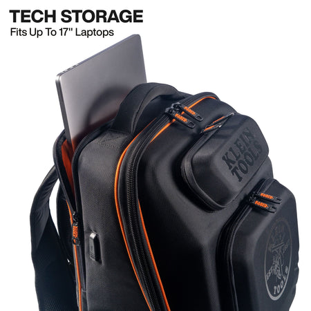 A black Klein Tools backpack with orange zipper accents, shown with a laptop partially inserted into the top storage pocket. Text in the upper left reads 'TECH STORAGE Fits Up To 17" Laptops'.