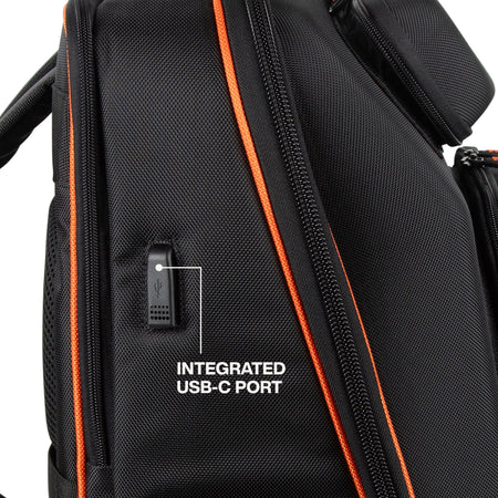 Close-up of a black backpack with orange zipper trim and a white text overlay pointing to an integrated USB-C port.
