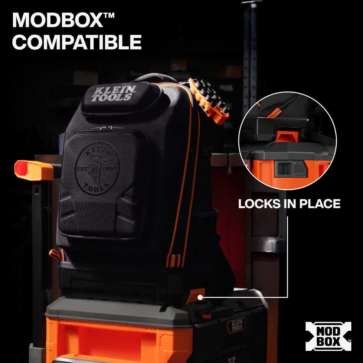 A black Klein Tools work bag with orange accents displayed on an orange and gray Modbox tool cart, with text reading 'MODBOX COMPATIBLE' and 'LOCKS IN PLACE' plus a circular inset showing the locking mechanism.