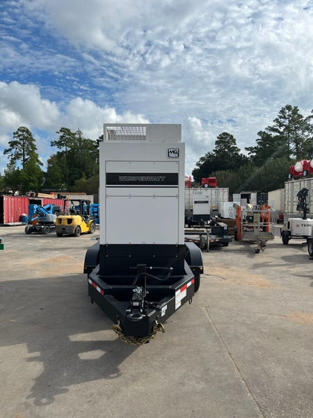  A white MQ Power "Whisperwatt" generator on a black trailer. The trailer has two wheels and a towing hitch, and the background shows other vehicles and some trees.