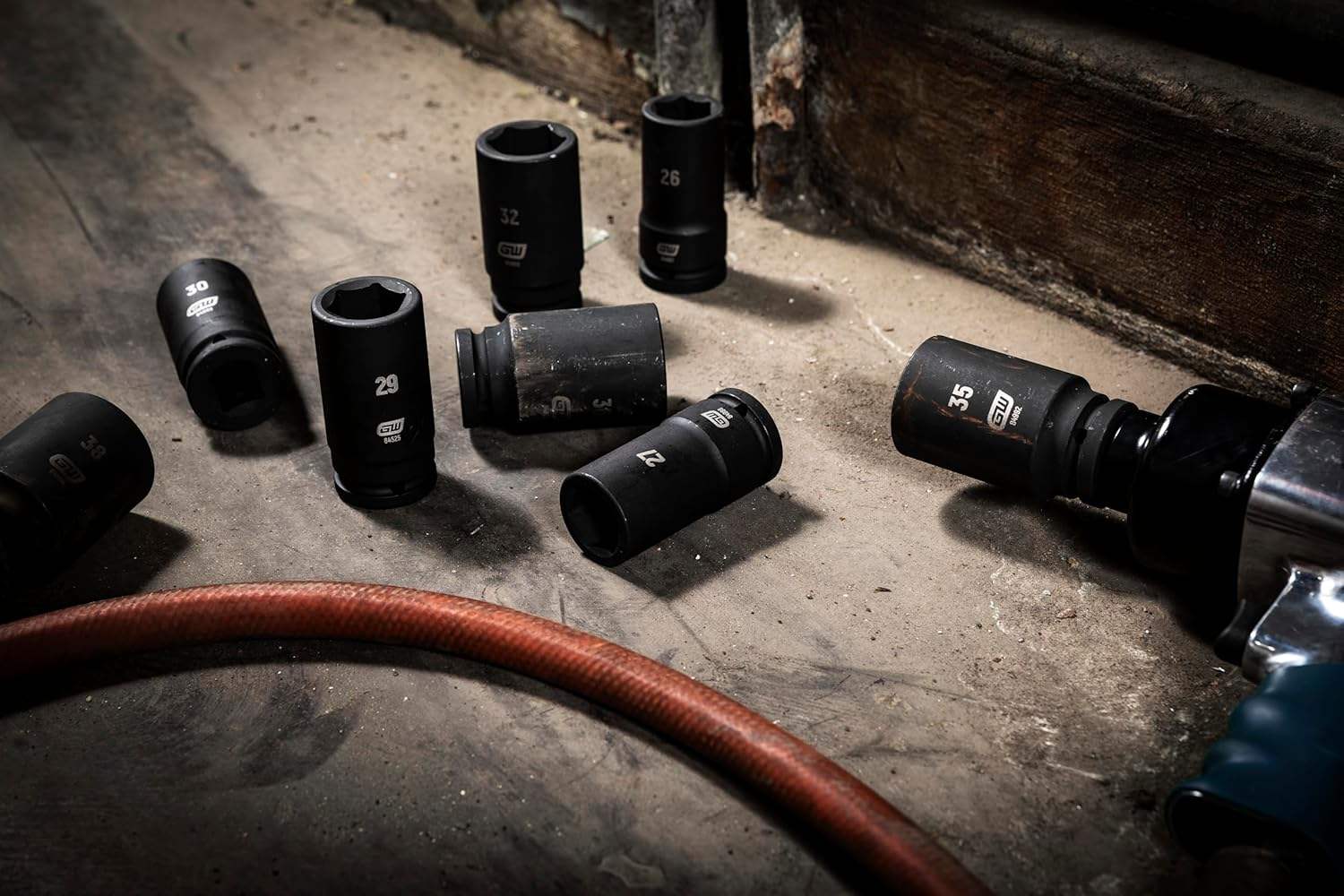 Several black GEARWRENCH 3/4-inch drive impact sockets are scattered on a concrete shop floor next to an air hose and an impact gun.