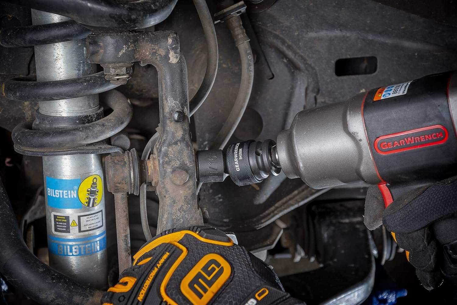 A gloved hand uses a GEARWRENCH 11/16-inch universal impact socket (84599N) with an impact wrench to remove a bolt from a vehicle's suspension assembly.