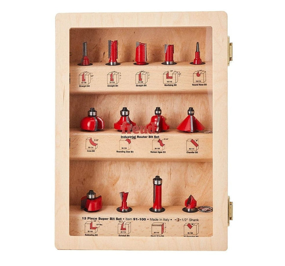 Freud 91-100 13 Piece Super Bit Set IN WOOD CASE. This is a wooden case with a clear plastic front, displaying a Freud 13-piece super router bit set. The set contains various router bits with silver shanks and red cutting heads, arranged on three shelves, each labeled with the bit type and a corresponding diagram.