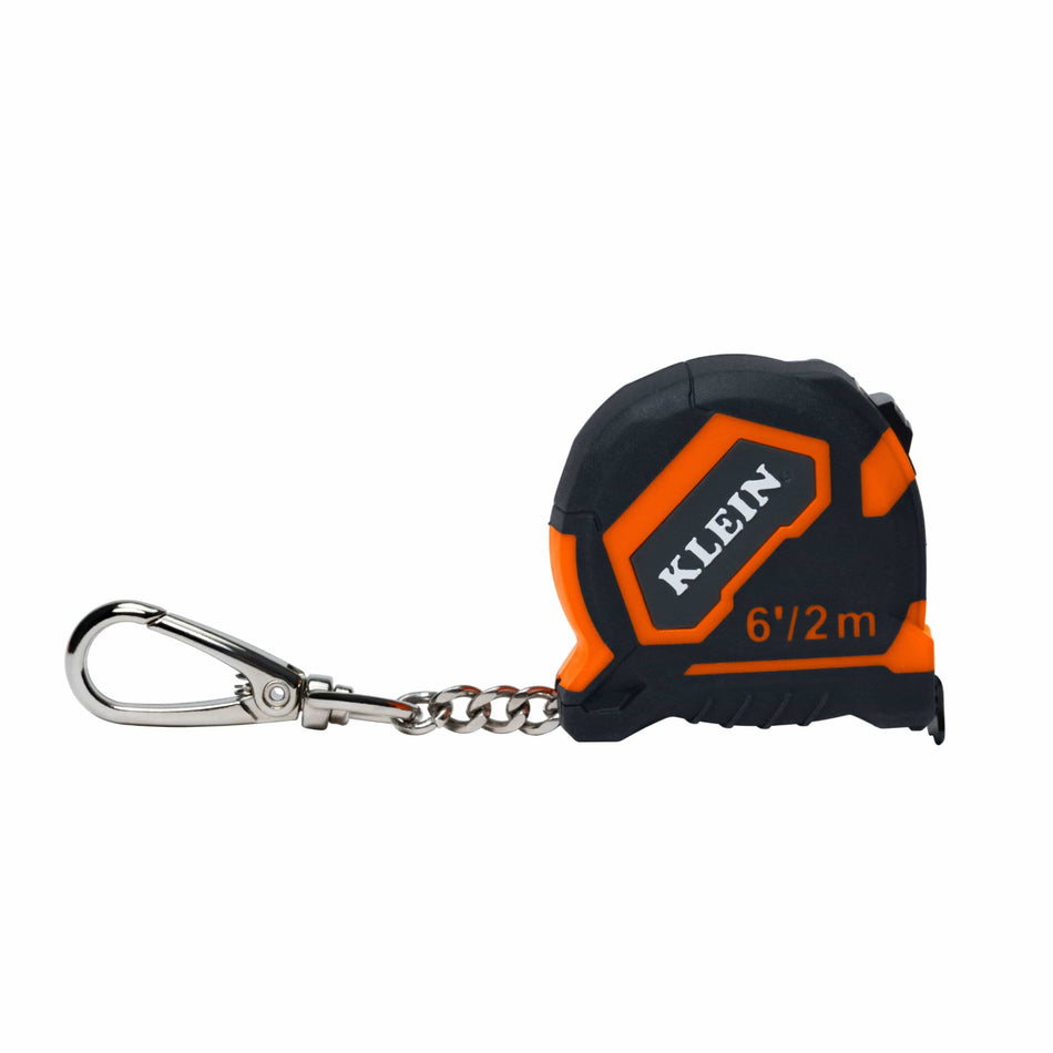A small Klein tape measure keychain with a black and orange casing, a silver carabiner, and a short metal chain on a plain white background.