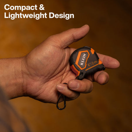 A hand holding a compact Klein tape measure with orange and black detailing against a warm brown background, with the text 'Compact & Lightweight Design' in the top left corner.