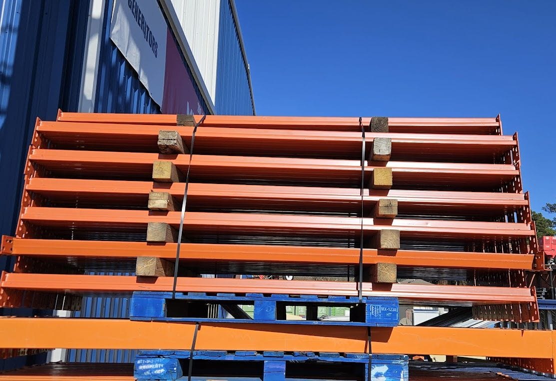 A large stack of industrial 8-foot teardrop pallet rack step beams in used like new condition, organized on blue pallets with wooden spacers and featuring a high-visibility safety orange powder-coated finish and 3-inch face height for heavy-duty warehouse storage racking.
