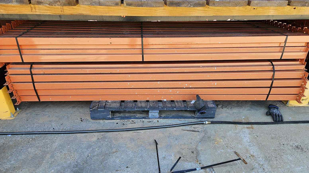 A wide-angle product photograph of multiple 9-foot industrial teardrop pallet rack step beams in like-new condition, showcasing the heavy-duty steel construction, 4.25-inch face height, and professional safety orange powder-coated finish for warehouse storage systems.