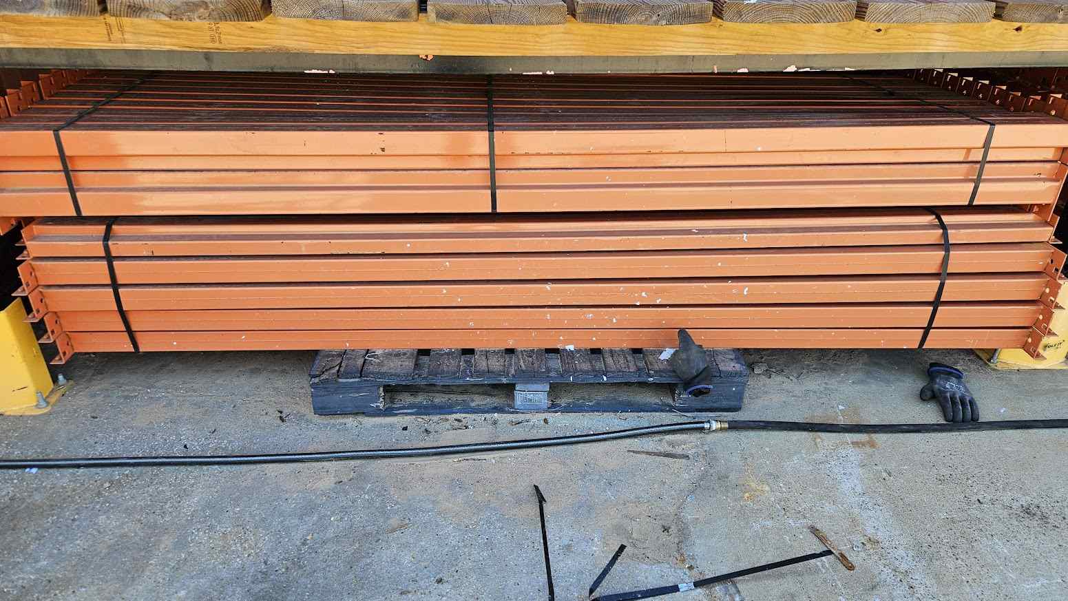 A wide-angle product photograph of multiple 9-foot industrial teardrop pallet rack step beams in like-new condition, showcasing the heavy-duty steel construction, 4.25-inch face height, and professional safety orange powder-coated finish for warehouse storage systems.