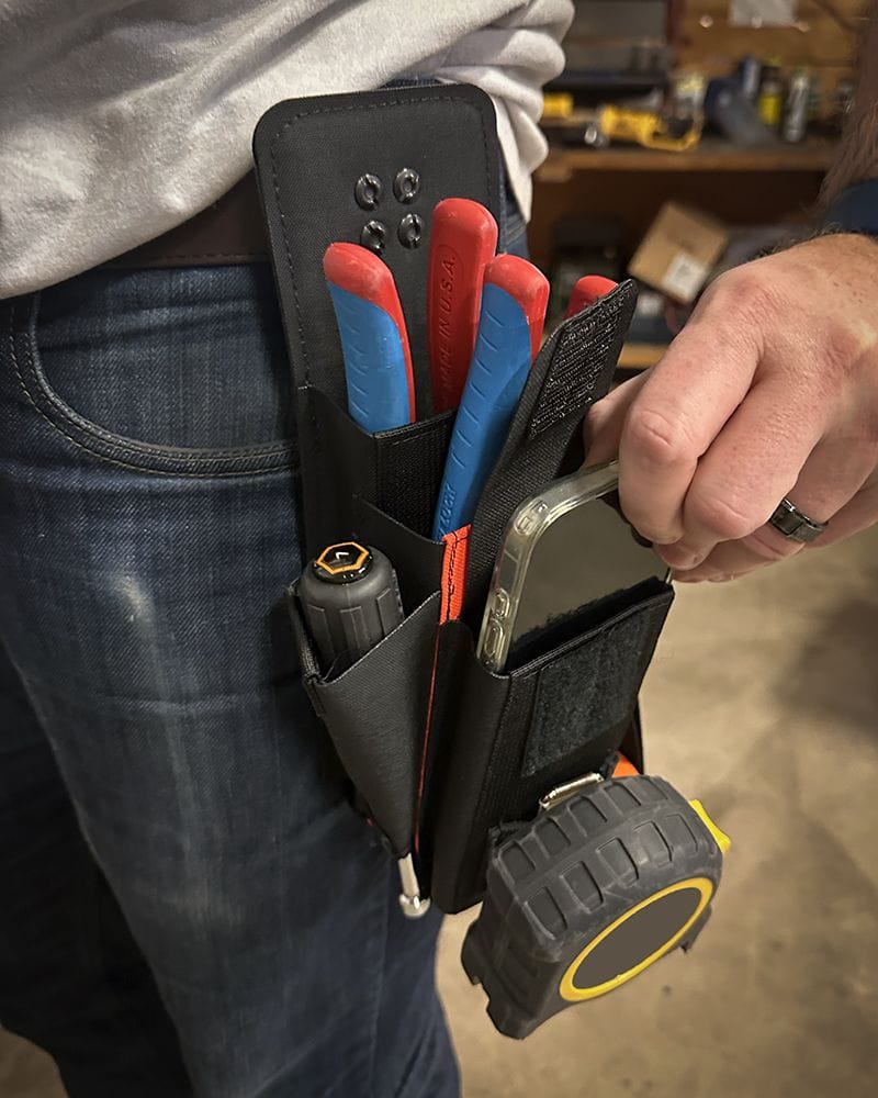 A close-up view of a trade professional wearing the black Atlas 46 utility belt pouch on blue jeans, with a hand removing a smartphone from the front compartment next to stored pliers and a tape measure.