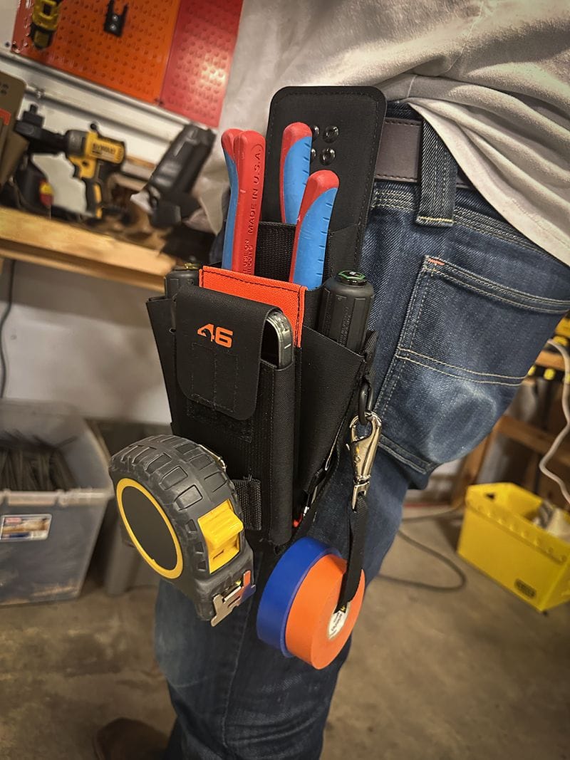 A side perspective of a technician on a jobsite wearing the Atlas 46 Murphy Speed Pouch Plus on a work belt, highlighting the snap carabiner attachment holding rolls of blue and orange electrical tape.