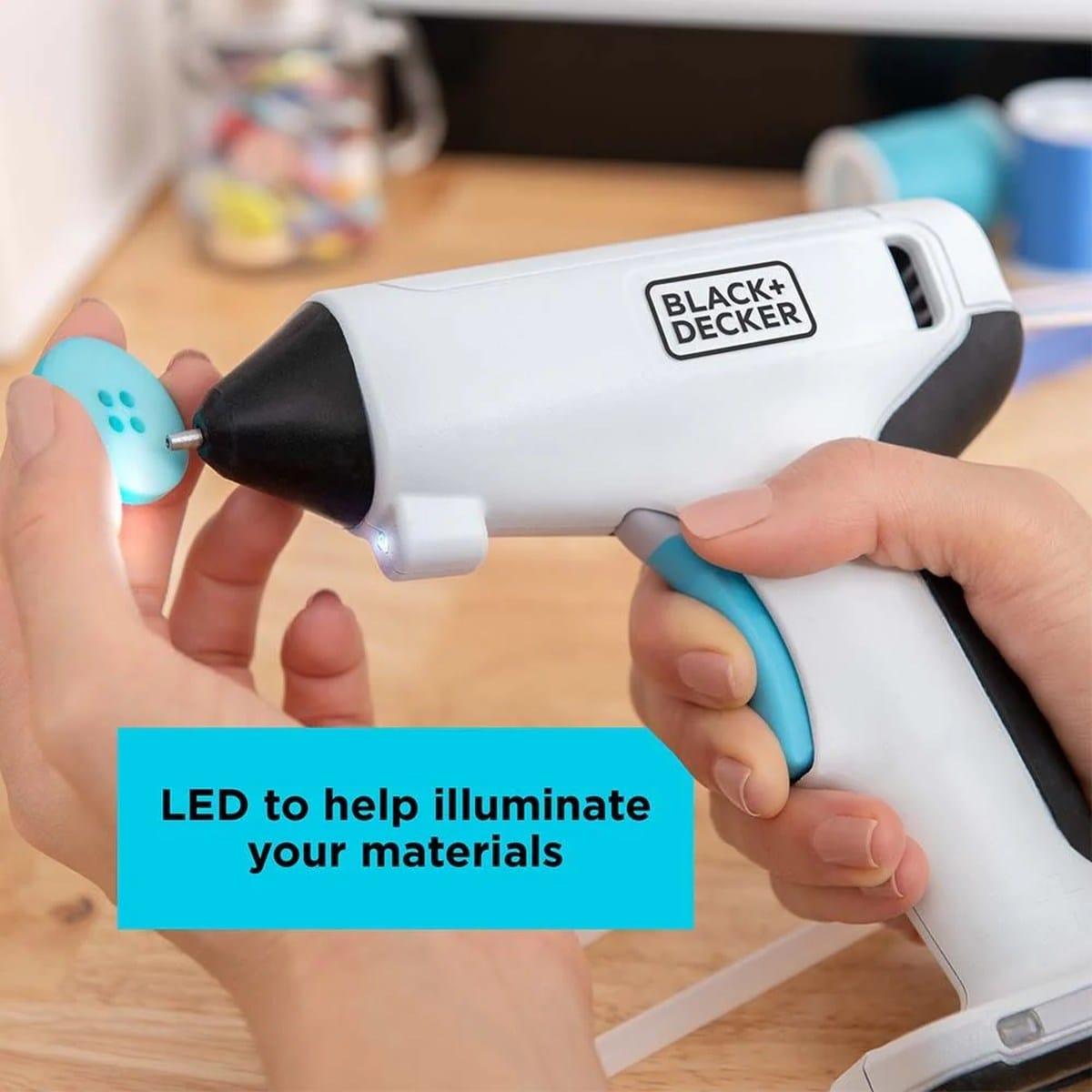 Person using the BLACK+DECKER 4V MAX cordless glue gun to apply adhesive to a craft button, demonstrating the helpful illuminating LED work light.