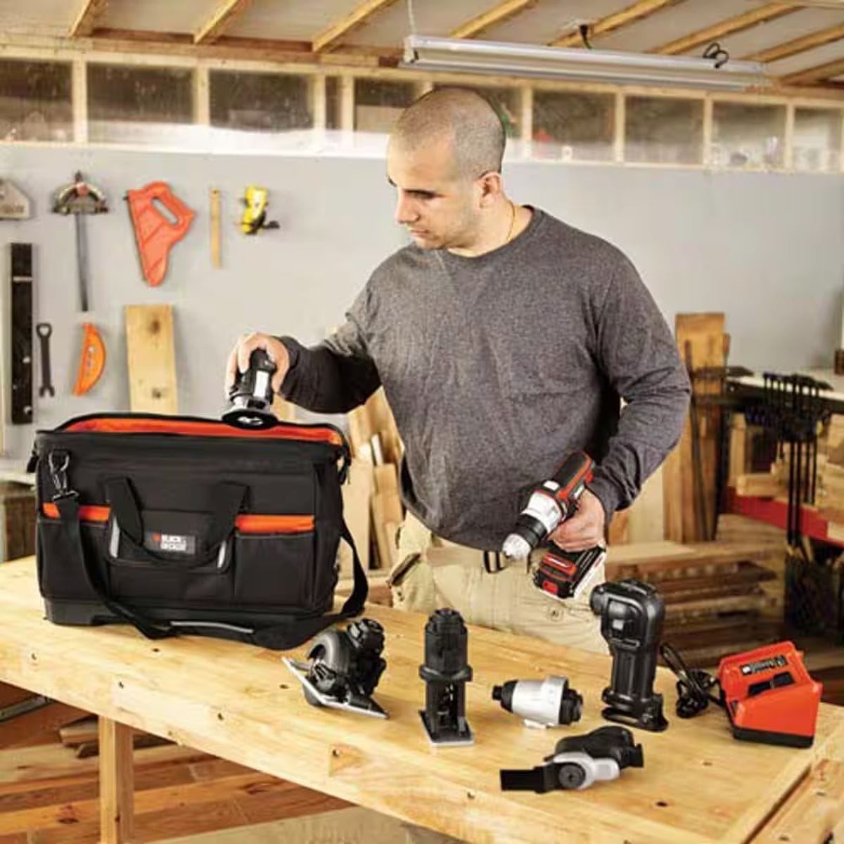A woodworker in a workshop environment organizing various Matrix system tool attachments on a workbench next to the open BLACK+DECKER 21-inch tool bag, highlighting the bag's large capacity and its role as a professional-grade multi-storage organizer.