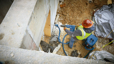Person using a drill in a construction setting with concrete and debris.