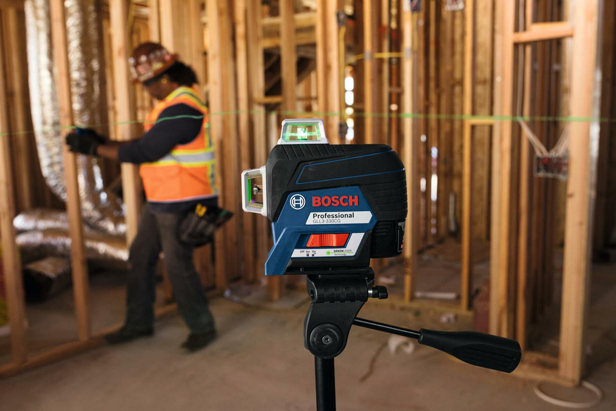 Bosch laser level mounted on tripod projecting green horizontal line across a framed construction site, used for accurate leveling during build.