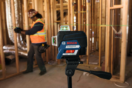 Bosch laser level mounted on tripod projecting green horizontal line across a framed construction site, used for accurate leveling during build.