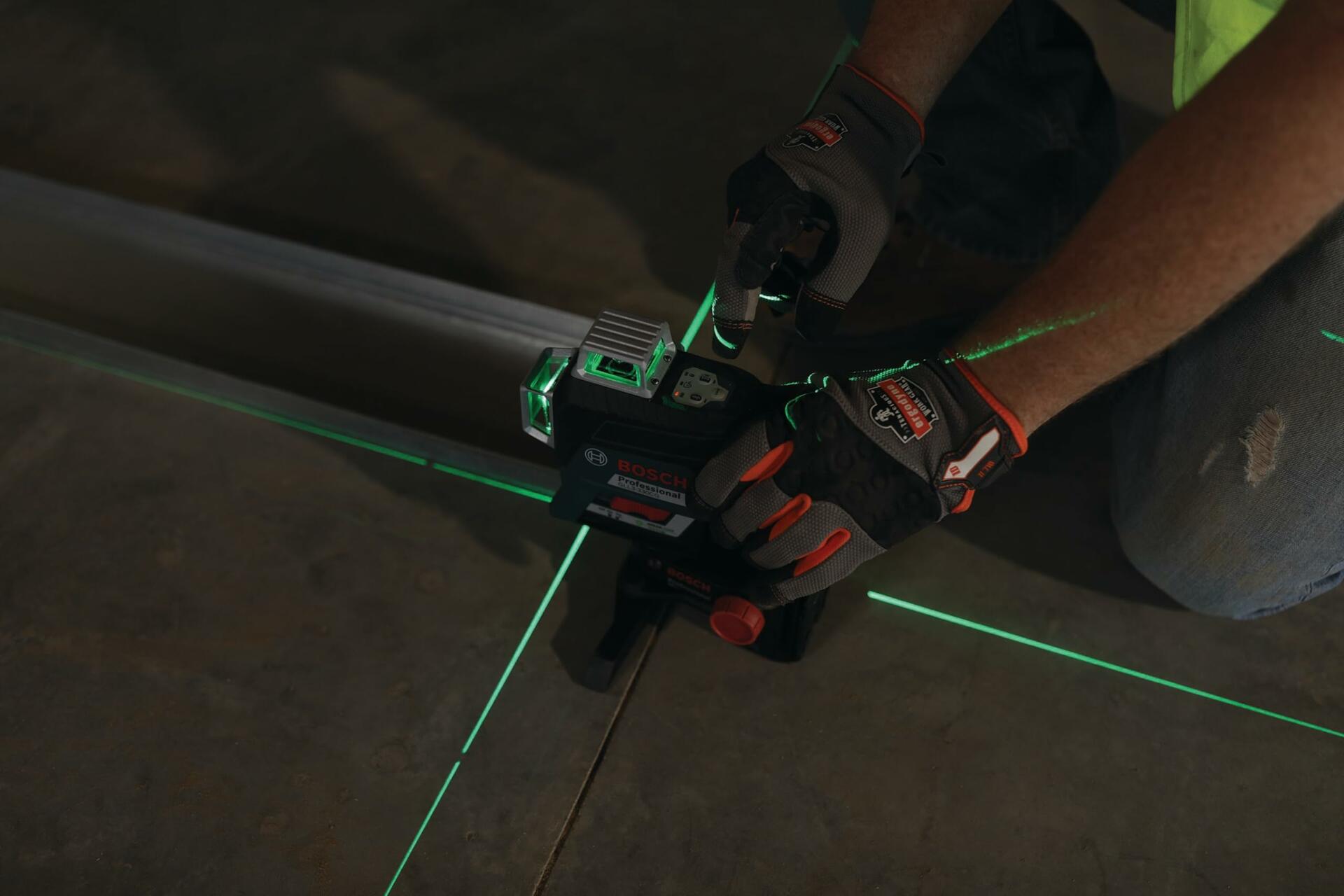 Person adjusting Bosch laser level on a concrete floor with green laser lines forming a cross, demonstrating tool use for precise layout.
