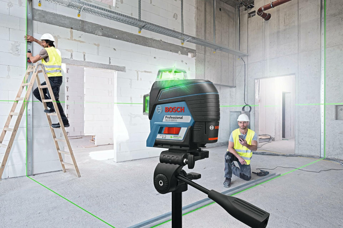 Two construction workers using Bosch laser level on a jobsite with green laser lines projected across walls and floor for vertical framing alignment