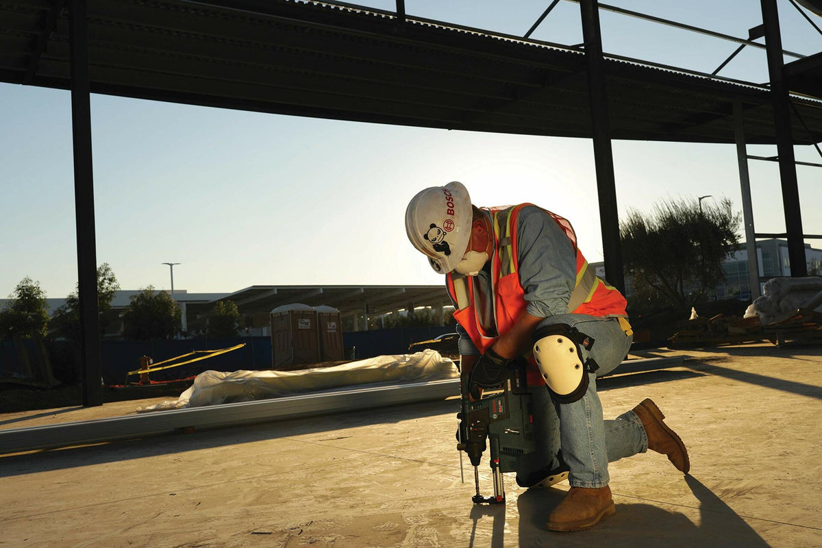 Person in safety gear working on a construction site with a clear sky.