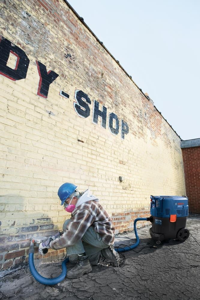 Wide shot of an industrial job site where a professional is using a BOSCH tuckpointing blade on a brick wall, demonstrating the efficiency of the diamond sandwich design in large-scale masonry renovation.