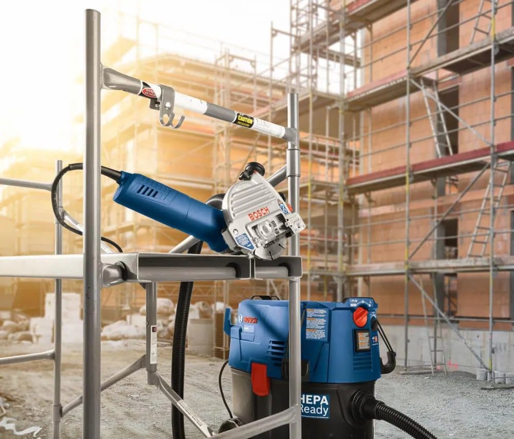 BOSCH masonry restoration setup on a construction site featuring a small angle grinder with a DD4510S diamond sandwich tuckpointing blade attached to a BOSCH HEPA-ready mobile dust extractor on scaffolding.