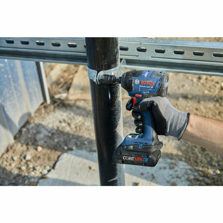 A gloved hand holding the Bosch GDR18V-1860C impact driver, tightening a pipe clamp onto a black vertical pipe with a metal fitting.