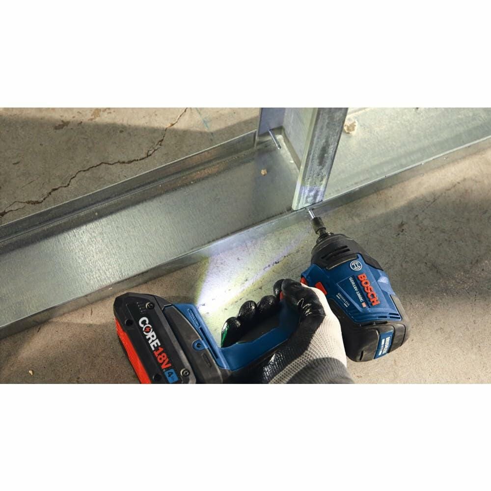 A gloved hand operating the Bosch GDR18V-1860C impact driver with an attached CORE18V battery, driving a screw into a metal stud during framing.