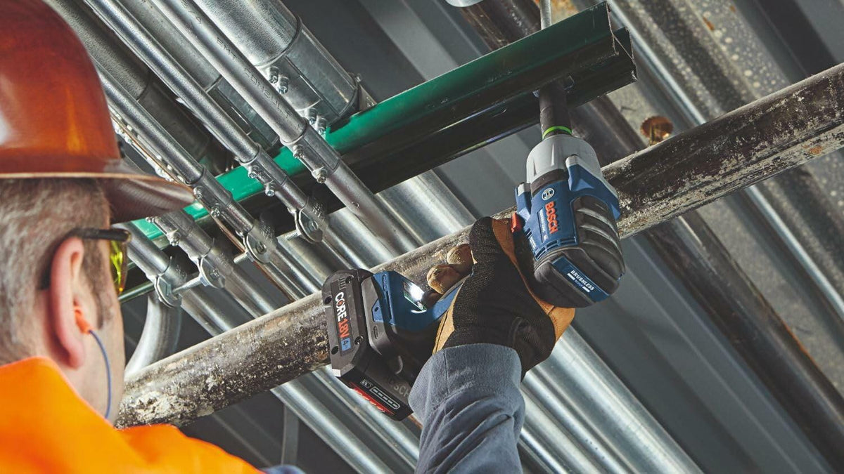 Worker in full safety gear using a Bosch GDS18V-330CN impact wrench on a metal pipe structure. The image highlights the tool’s ergonomic design and cordless convenience in a construction or industrial setting.