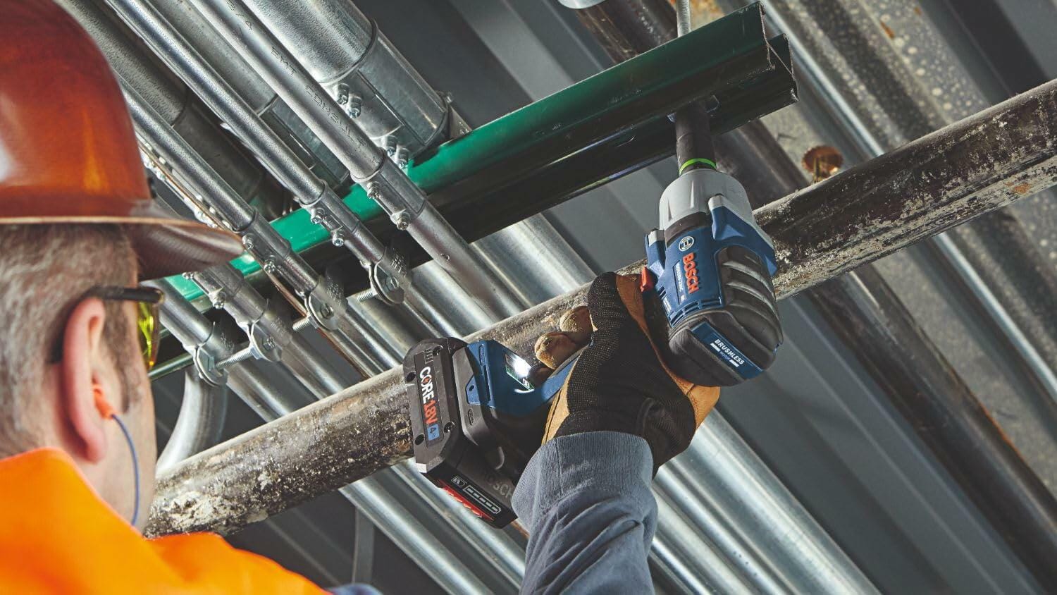 Worker in full safety gear using a Bosch GDS18V-330CN impact wrench on a metal pipe structure. The image highlights the tool’s ergonomic design and cordless convenience in a construction or industrial setting.