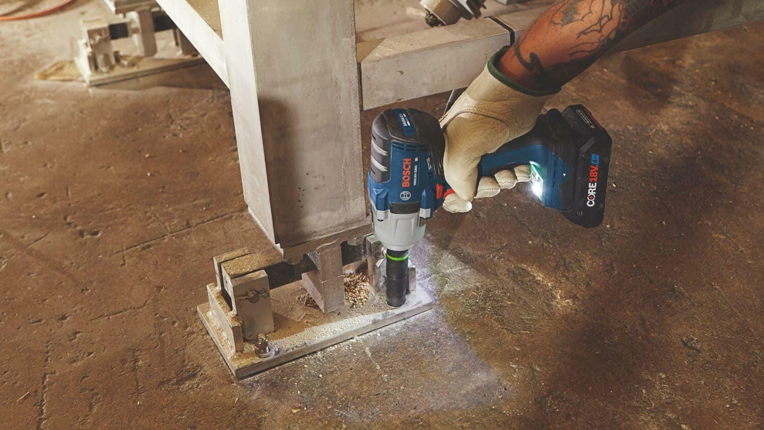 Person using a Bosch GDS18V-330CN cordless impact wrench to tighten bolts on an industrial pipe system. The tool features a CORE18V battery and brushless motor, and the user wears gloves and a high-visibility vest, demonstrating safe operation in a mechanical work environment.