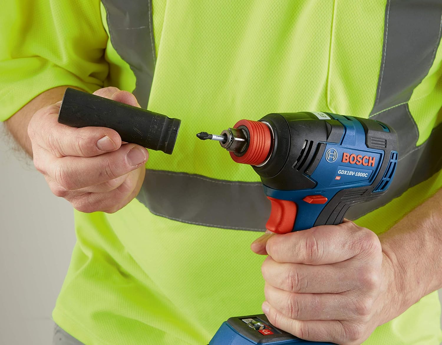 Worker in high‑visibility gear holding a Bosch GDX18V‑1800C reconditioned 18V brushless impact driver and socket attachment, demonstrating tool readiness for professional fastening and mechanical applications.