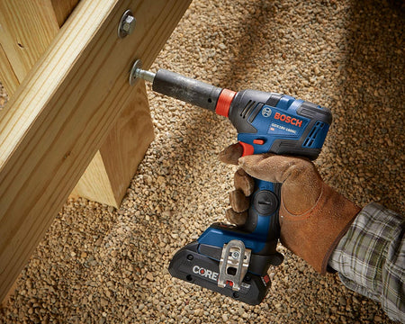 Gloved hand using the Bosch GDX18V‑1800C reconditioned 18V brushless impact driver to tighten a large bolt into a wooden structure, showcasing high‑torque performance in construction settings.