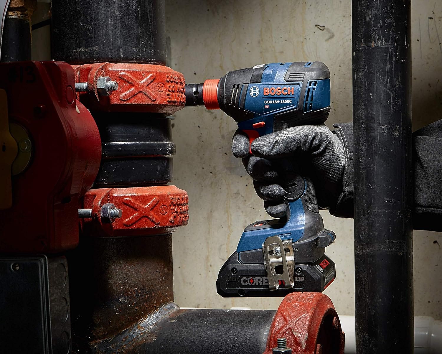 Close‑up of a gloved worker using the Bosch GDX18V‑1800C reconditioned 18V brushless impact driver on industrial pipe couplings, highlighting torque strength and reliability in mechanical installations.