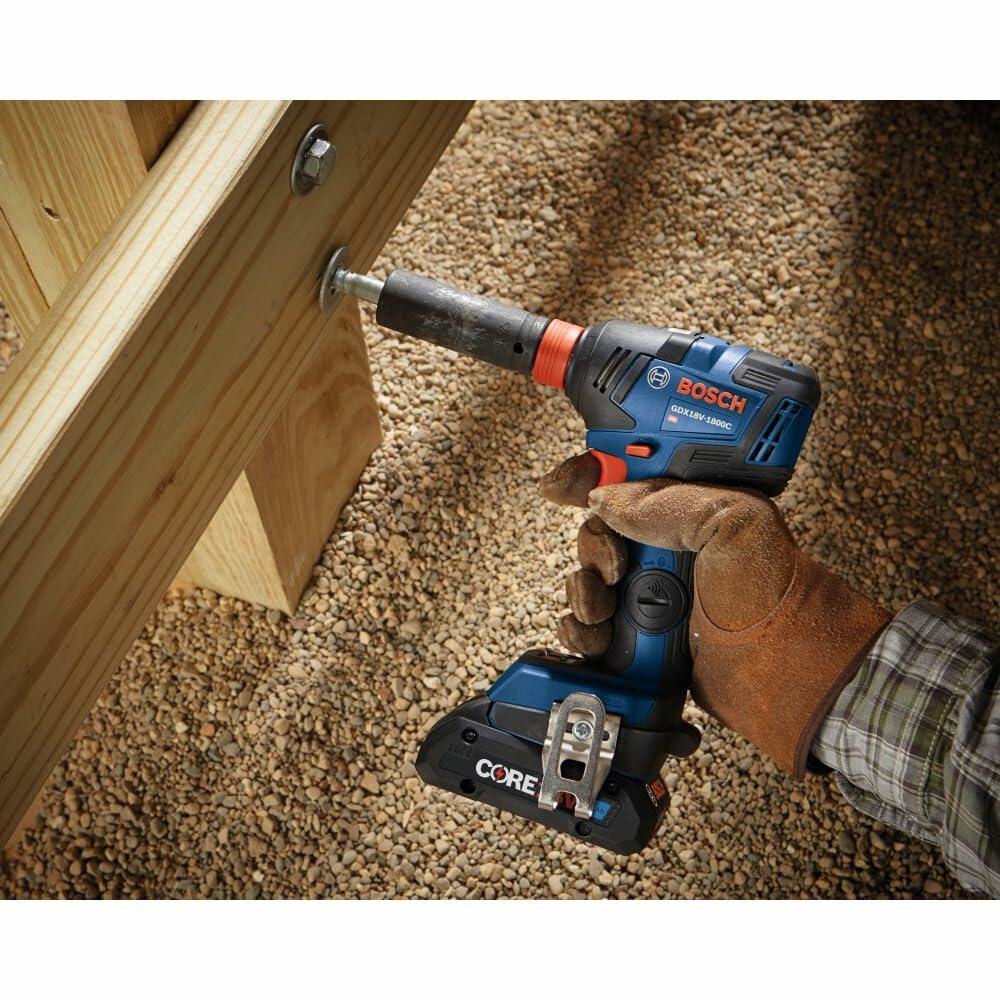 Close-up of a Bosch cordless drill driving a screw into a vertical wooden surface. The drill is equipped with a red CORE18V battery and belt clip, used in an indoor construction setting.