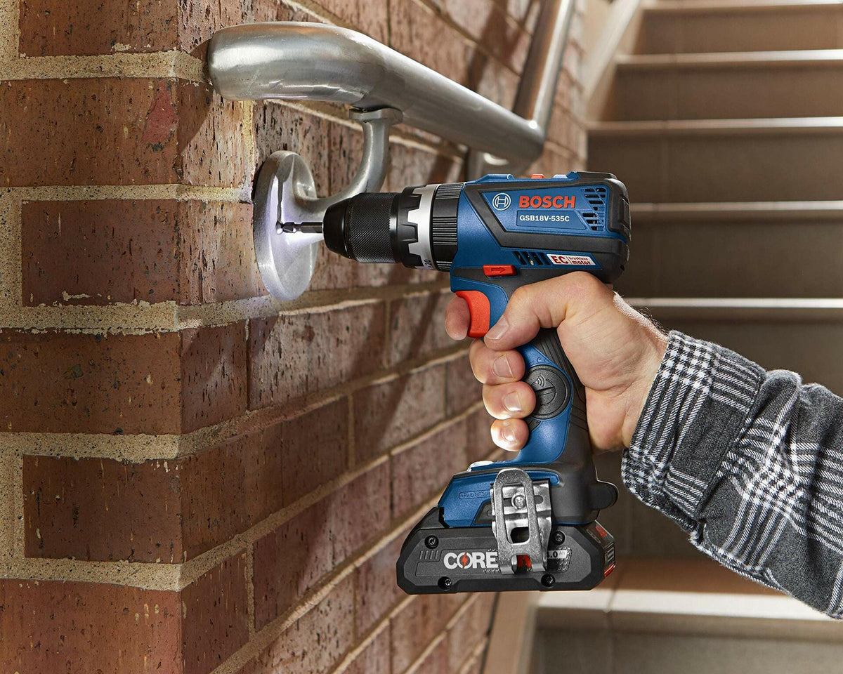 Person using a Bosch GSR18V-535C cordless drill to install a metal handrail bracket into a brick wall. Drill is equipped with a CORE18V battery. Scene highlights tool’s capability for drilling into metal and masonry surfaces during stairway construction.