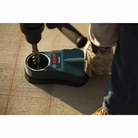 Worker using Bosch HDC200 dust collection attachment with drill on concrete surface; attachment pressed flat against wall with drill bit inserted, showcasing dust capture in action.