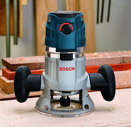 Bosch MRF23EVS router placed on a workbench surrounded by wood shavings. The red dial on the front allows for speed or depth adjustment. Black handles and a flat base provide control and stability during use.
